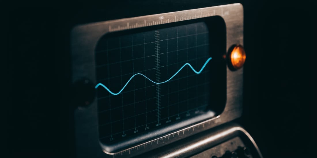 An oscilloscope screen in the dark: a single cyan trace across an etched graticule, in a brushed aluminium bezel with an amber pilot lamp beside it.